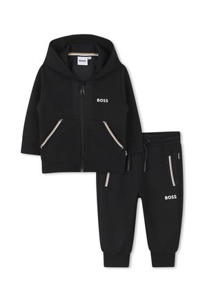 Sudadera negra para niño pequeño con capucha y cremallera y pantalones jogger a juego, ambos con bolsillos delanteros y logo blanco "BOSS" en el pecho y la pierna.