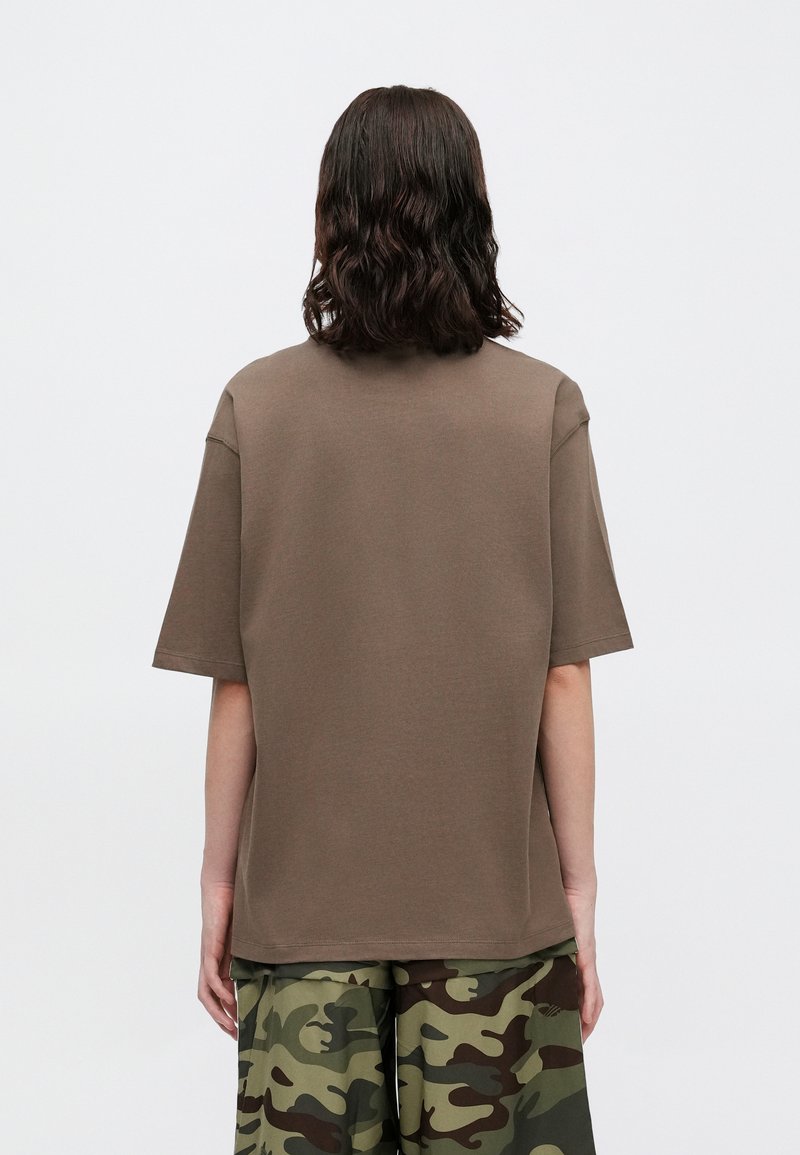 Braunes Baumwoll-T-Shirt mit Rundhalsausschnitt, kurzen Ärmeln und lockerer Passform. Getragen mit grünen Camouflage-Hosen.