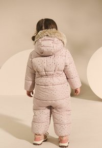 Gevoerde roze sneeuwpak met een pluche bontvoering bij de capuchon, voorzien van metalen sterrenpatronen. Dikke, geïsoleerde stof voor warmte en comfort.
