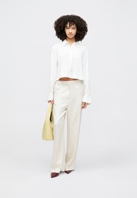 White cropped button-up shirt, beige wide-leg trousers, and a yellow bag. Model wears pointed burgundy heels, with a smooth textured finish.
