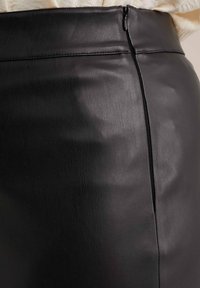 Melnā aitas ādas svārki ar gludu tekstūru, augsto jostasvietu un diskrētu rāvējslēdzēja detaļu aizmugurē. Minimalistisks dizains ar elegantu siluetu.