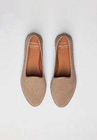 Beige suede slip-on shoes with a rounded toe, elastic trim, and textured stitching. Labeled "Woman by Fred Martin, Made in Spain."