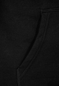 Tessuto di cotone nero con una texture liscia, caratterizzato da un dettaglio di cucitura della tasca, che enfatizza un design pulito e minimale.