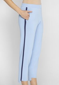Jasnoniebieskie spodnie z ryflowanej tkaniny, z granatowym paskiem po boku oraz kieszenią po prawej stronie, o długości 3/4.