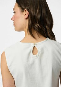 Balta kokvilnas bezpiedurkņu blūze ar noapaļotu kakla izgriezumu un atslēgas caurumu aizmugurē, ar mīkstu, gludu tekstūru.