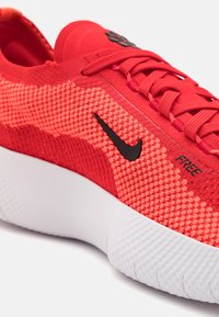 Rød atletisk sko med en teksturert strikket overdel, svart Nike-logo og en hvit polstret såle med et unikt mønster.