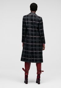 Cappotto a quadri bianco e nero con vestibilità su misura, maniche lunghe e design a mezza lunghezza, abbinato a stivali bordeaux alti fino al ginocchio con lacci.