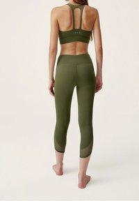 Olivgrünes Sportset mit einem croptop im Racerback-Design und passenden hochtaillierten Leggings mit Mesh-Details an den Waden.