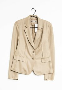 Beige propracovaný blazer s klopovým límcem, dvěma předními kapsami, dvěma knoflíkovými zapínáními a hladkou strukturou. Visí na černém háčku.