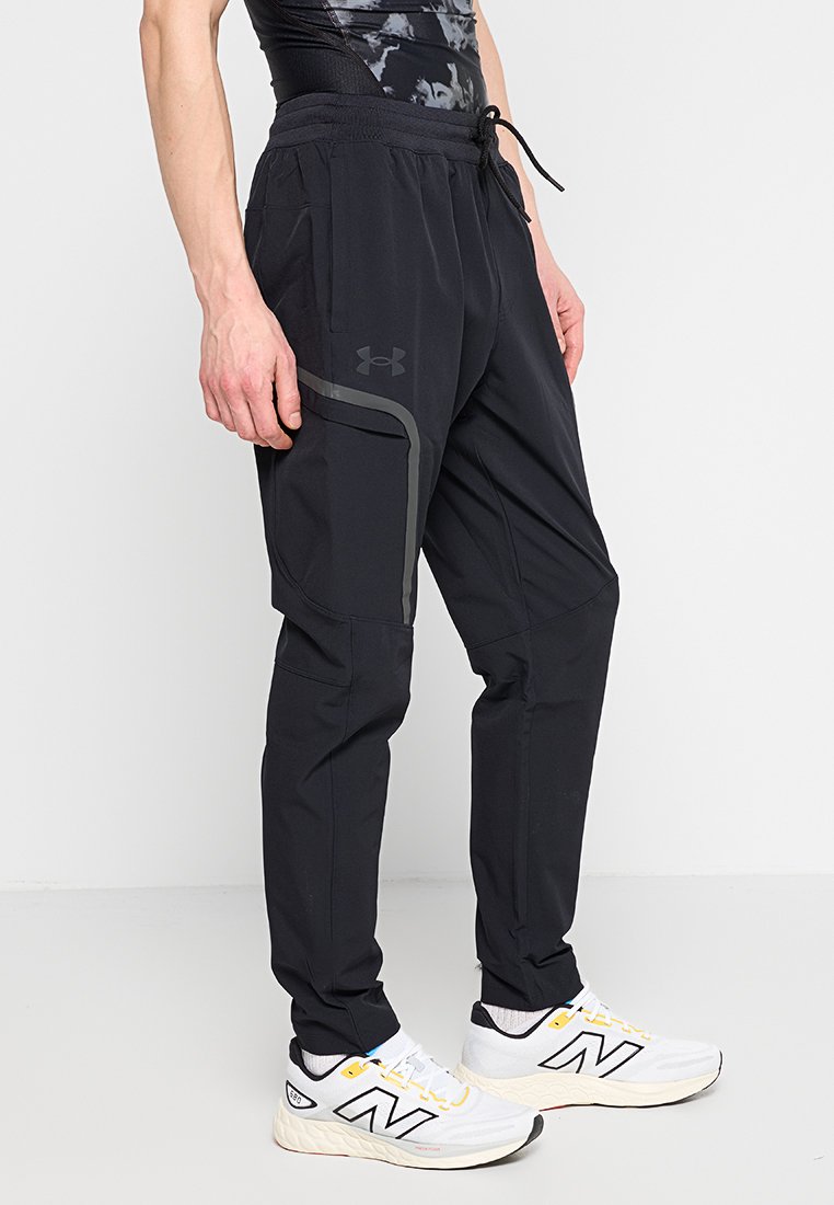 Pantalones deportivos negros con cintura ajustable mediante cordón, bolsillos con cremallera y detalles grises. Fabricados con un tejido ligero y elástico para mayor comodidad y movilidad.