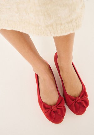 Rote Wildleder-Ballerinas mit einer runden Zehenpartie und einer markanten Schleifendetail vorne. Glatte Textur und flaches Design.