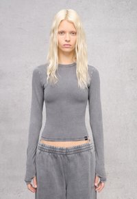 Maglia grigia a maniche lunghe in materiale morbido ed elasticizzato, con una silhouette aderente e una sottile texture a coste. Abbinata a pantaloni grigi coordinati.