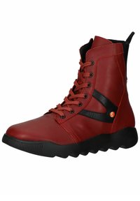 Botín de cuero rojo con detalles en negro, diseño de cordones, puntera redondeada y suela de goma texturizada con un patrón de zigzag.