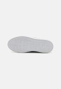 Vit sneakersula med präglad "GUESS" logotyp, slät yta, rund tå och hållbart gummimaterial. Ren och minimalistisk design.