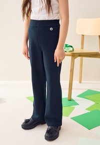 Pantalones de pierna ancha color azul marino hechos de tela suave, con un pequeño detalle de flor plateada en la cintura. Combinados con mocasines negros.