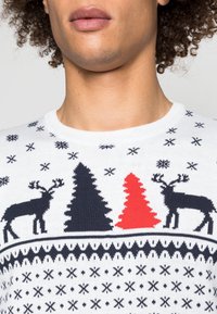 Maglione bianco lavorato a maglia con motivo di renne rosse e nere, alberi verdi scuri e rossi, e motivi di fiocchi di neve sull'intera superficie.