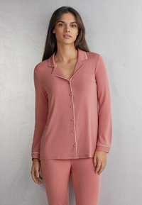 Růžový pyžamový set s dlouhým rukávem, knoflíkovým zapínáním, bílým lemováním na límci a manžetách, hladkou tkaninou a volným střihem.