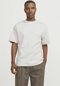 Lysegrå kortærmet t-shirt lavet af bomuld med en afslappet pasform og en rund halsudskæring. Har et minimalistisk tekstlogo på brystet.