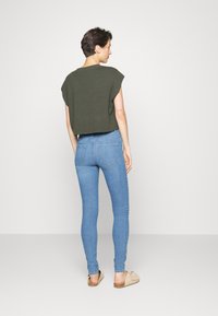Rövid ujjú, cropped zöld pulóver könnyű kék skinny farmernadrággal párosítva. Az öltözet egyszerű, letisztult kialakítással és minimális részletezéssel rendelkezik.