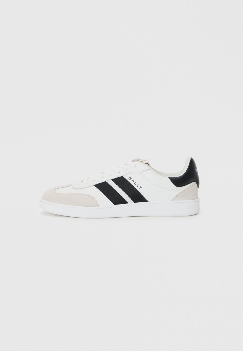 Sneaker alb cu dungi negre, accente moi din suede bej și talpă din cauciuc alb. Are un design cu șireturi și logo-ul mărcii pe lateral.