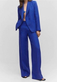 Helderblauw op maat gemaakt blazer en wijde broek in gestructureerde stof. Het blazer heeft een sluiting met twee knopen en notch revers.