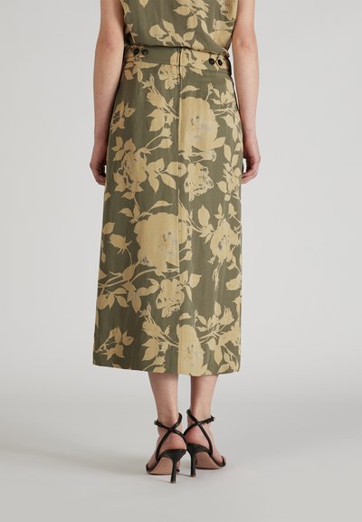 Jupe midi florale vert olive avec des roses beiges, dotée de boutons à la taille et d'une silhouette droite. Portée avec des talons sangle noirs.