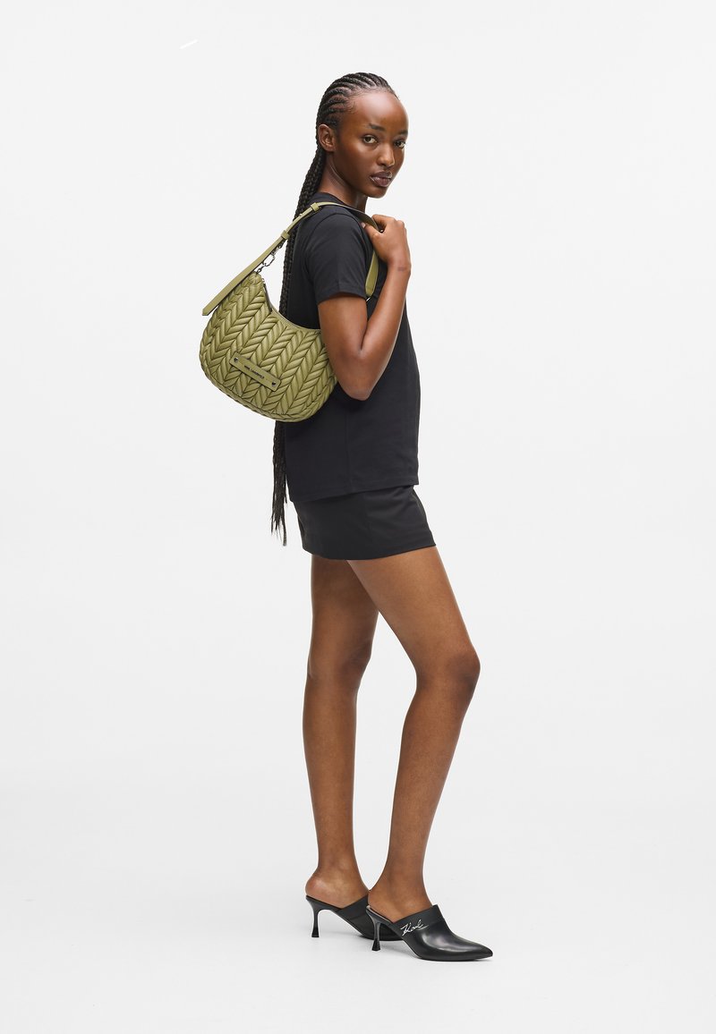 Grønn vevd hobo-veske med et strukturert mønster, kort stropp og flat bunn, kombinert med en svart t-skjorte og mini-shorts.