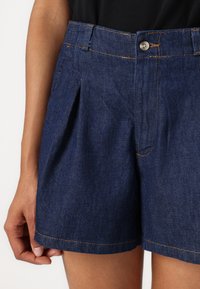 Denimske kratke hlače v temno modri barvi z udobnim krojem, s skrito sprednjo plisirano obliko, petimi žepi in kontrastnim oranžnim šivom.