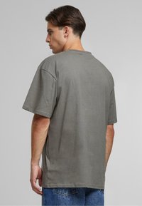 T-shirt en coton gris à manches courtes, col rond, coupe décontractée et ourlet droit. Porté avec un jean en denim bleu. Vue de dos montrée.