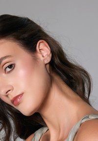 Srebrne kolczyki wkrętki na modelce z długimi brązowymi włosami. Kolczyki są małe, okrągłe i mają minimalistyczny design.