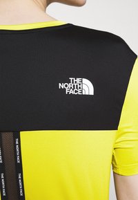 Czarna i żółta koszulka z krótkim rękawem z logo The North Face na górnej części pleców oraz markowym czarnym paskiem z siatki biegnącym pionowo.