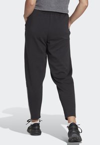 Pantalones de chándal negros con un ajuste ajustado, cintura elástica, bolsillos laterales y rayas blancas en los lados. La tela parece suave y flexible.