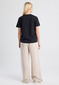 Black cotton t-shirt with short sleeves, crew neck, and relaxed fit paired with light beige striped wide-leg pants.