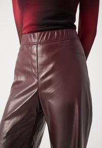 Bordeaux leren broek met een soepele textuur, voorzien van een elastische tailleband en zijnaad, met een strakke pasvorm en glanzende afwerking.