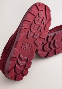 Calzature in camoscio bordeaux con suola in gomma testurizzata, caratterizzata da un battistrada a zigzag. Il logo è impresso sulla suola.