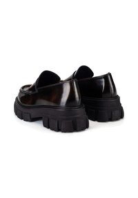 Brązowe, wypolerowane mokasyny ze skóry z masywną czarną gumową podeszwą i zaokrąglonym noskiem. Subtelne przeszycia na cholewce i niska linia cięcia.