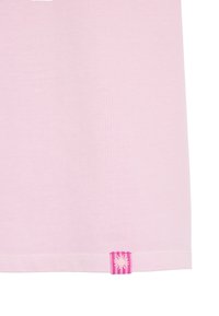 Jasnoróżowa bawełniana koszulka z płaskim dołem i małą, paskowaną różową metką z białym emblematem słońca w dolnym lewym rogu.