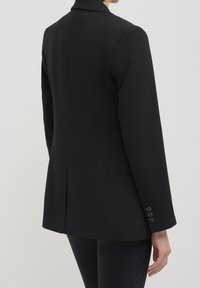 Blazer noir avec une silhouette structurée, des revers crantés et des manches longues avec des accents de boutons. Tissu lisse et coupe ajustée.