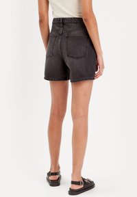 Hoge taille zwarte denim shorts met een verweerde textuur, voorzien van klassieke achterzakken en een afgewerkte zoom. Gemaakt in combinatie met zwarte sandalen.