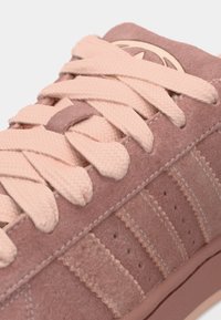 Ružové semišové tenisky s textúrovanými šnúrkami, vertikálnymi pruhmi a jemnými detailmi prešitia. Na jazyku sa nachádza logo. Hladká gumová podrážka.