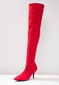 Botte à talon aiguille en daim rouge montant jusqu'au genou, avec un bout pointu. La tige est lisse, sans éléments métalliques visibles ni motifs, présentant un design épuré.