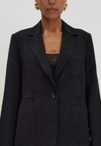 Zwarte linnen blazer met een notch-reep, enkele knoopsluiting en twee voorzakken. Heeft een gestructureerde pasvorm en subtiele textuur.