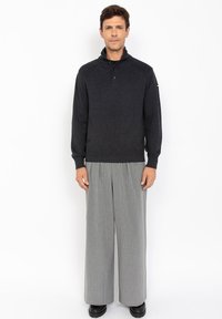 Ciemnoszary sweter z wysokim kołnierzem i prążkowaną teksturą, w połączeniu z szerokimi spodniami w szare pionowe paski. Czarne buty dopełniają całość.