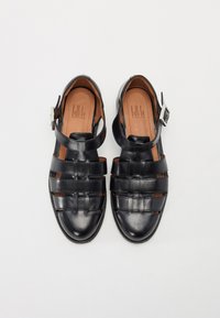 Black leather sandals with woven design, open toe, and ankle strap. Features a smooth finish and a brown leather insole. Adjustable buckle closure.