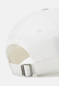Baltas reguliuojamas kepurė, pagaminta iš medvilnės, su išlenktu kraštu, siuvinėjimu ir metaliniu užsegimu gale.