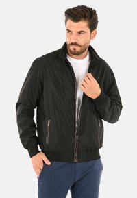 Giacca bomber nera con frontale zip, due tasche laterali, polsini e orlo a coste, con cuciture a contrasto lungo il colletto.