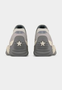 Ζευγάρι μπεζ και γκρι αθλητικά παπούτσια που φαίνονται από πίσω, με παχιά σόλα και αστέρι σχεδιασμένο σε κάθε τακούνι.