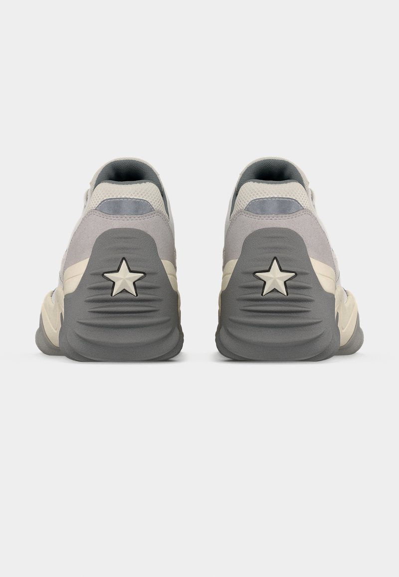 Coppia di sneakers beige e grigie viste da dietro, con suole spesse e un motivo a stella su ogni tallone.