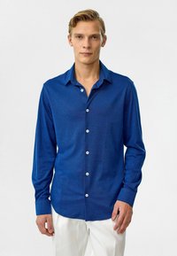 Blauw langarm shirt van gestructureerde stof, met een knoopsluiting aan de voorkant en witte knopen, aangevuld met een puntige kraag.