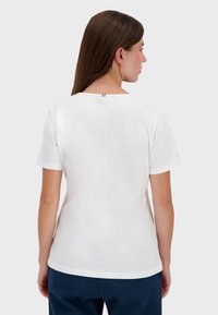 Bílý krátký rukáv tričko, kulatý výstřih, měkká bavlněná látka, s malým modrým, bílým a červeným akcentem na zadním límci.